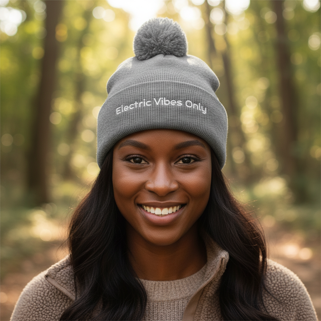 Straight-on headshot of woman with dark skin wearing heather grey pom pom Electric Vibes Only beanie
